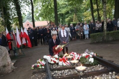 Na zdjęciu klęczący mężczyzna składający kwiaty pod pomnikiem. Obok niego stoi harcerka