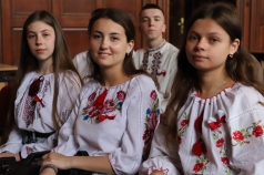 Grupa uczniów w strojach ludowych Ukrainy siedzi w auli.