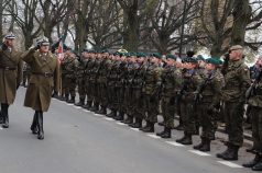 Po prawej grupa stojących żołnierzy. Po lewej idzie dwóch salutujących oficerów.