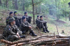 Grupa uczniów w żołnierskich mundurach siedzi na polanie.