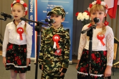 Dwie dziewczynki śpiewają. W środku stoi chłopiec w mundurze żołnierza.