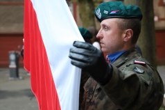Mężczyzna w mundurze wojskowym trzyma flagę biało-czerwoną.