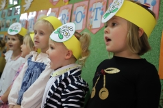 Na zdjęciu pięć śpiewających dziewczynek. Dziewczynki mają na głowie żółtą opaskę a na niej doczepiony rysunek stokrotki