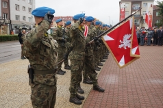 Na zdjęciu salutujący żołnierze. Jeden z nich trzyma w ręku sztandar w wizerunkiem Orła Białego