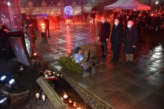 Żołnierz składa pod pomnikiem wieniec. Za nim stoi trzech mężczyzn.