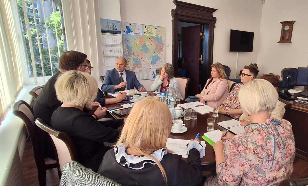 grupa osób w gabinecie Zachodniopomorskiego Kuratora Oświaty siedzi przy stole, rozmawia